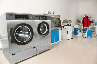 Waschküche mit grossen Industriewaschmaschinen, blauen Schränken und Kleiderstangen.