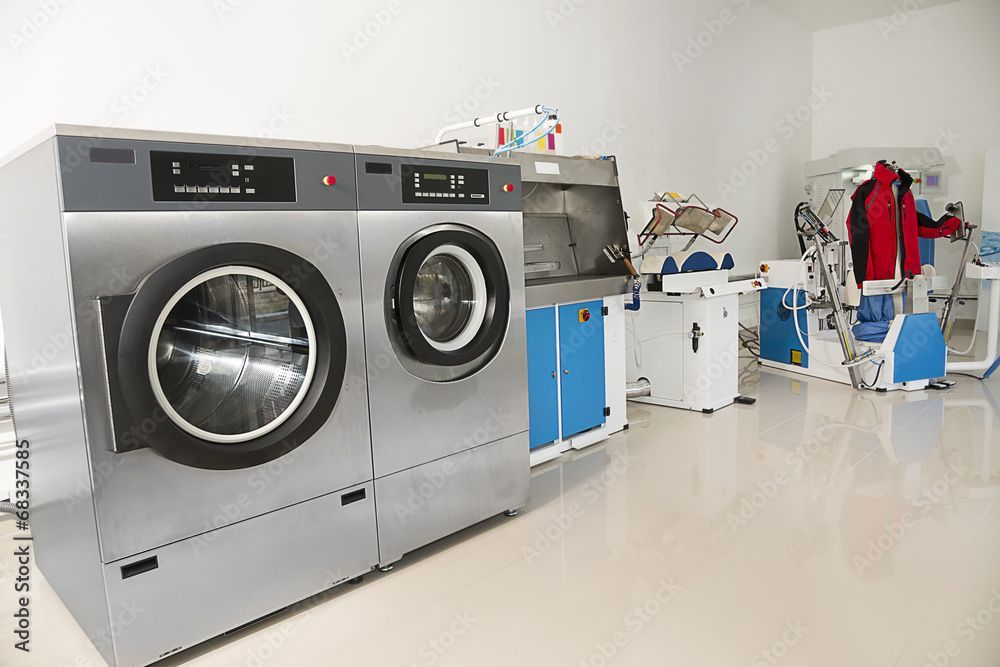 Waschküche mit grossen Industriewaschmaschinen, blauen Schränken und Kleiderstangen.