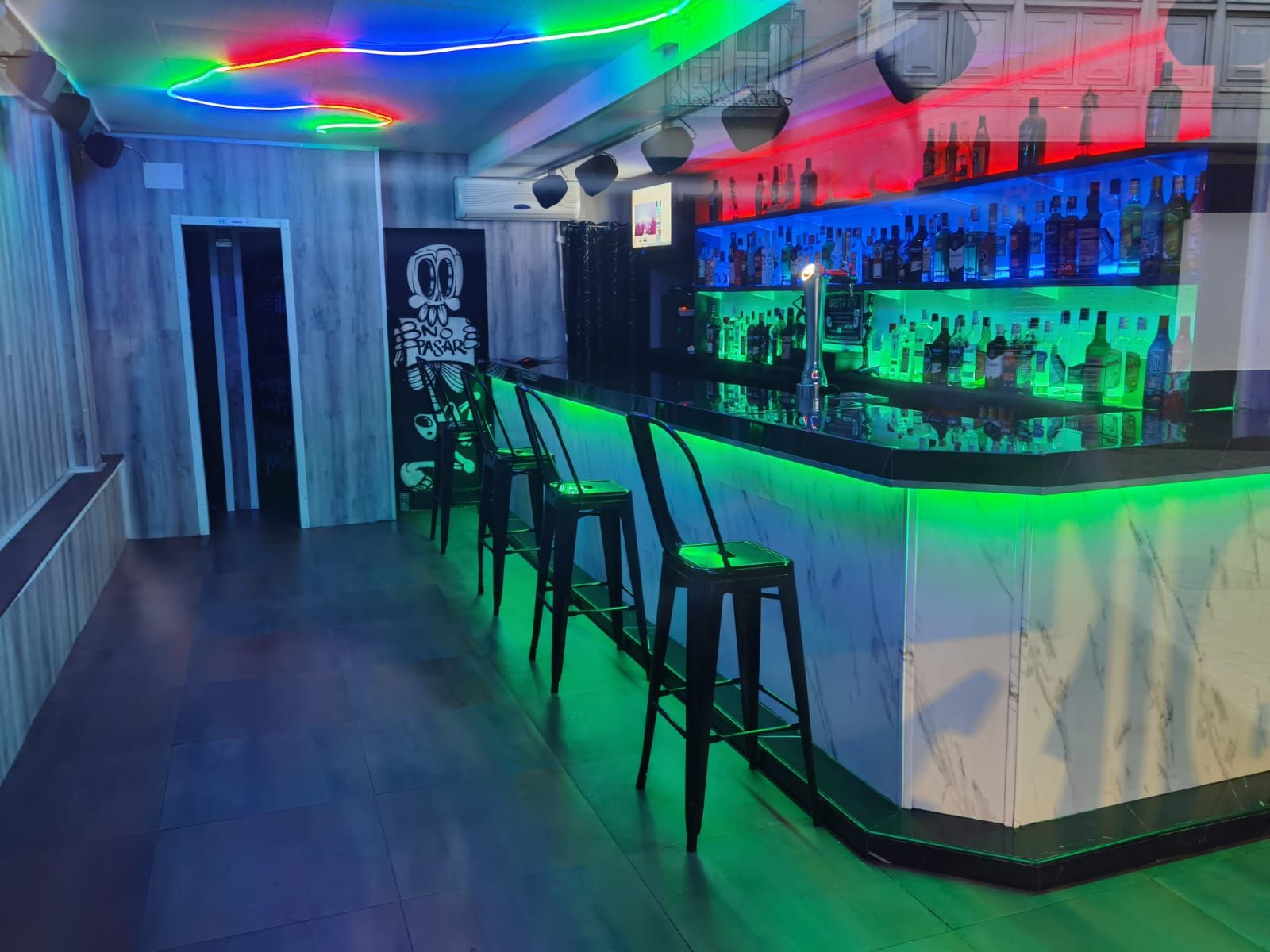 Interior del bar con iluminación verde neón en la barra y el techo.