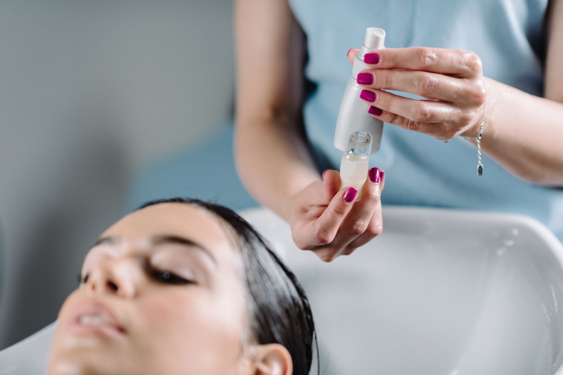 Mujer lavándose el cabello en un salón; el estilista sostiene un producto.
