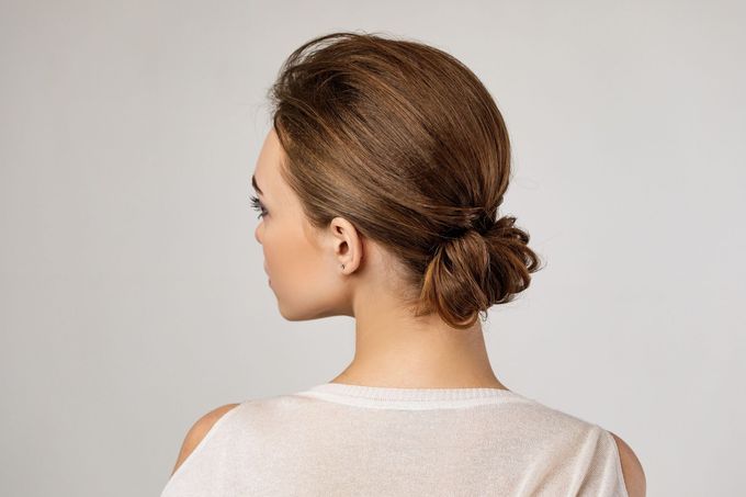 Mujer con cabello castaño claro recogido en un moño bajo, con un top blanco, vista de perfil.