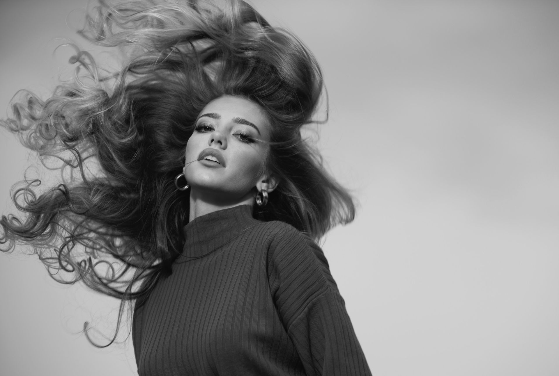 Mujer con cabello largo recogido, con suéter de cuello alto, mirando a la cámara. Blanco y negro.