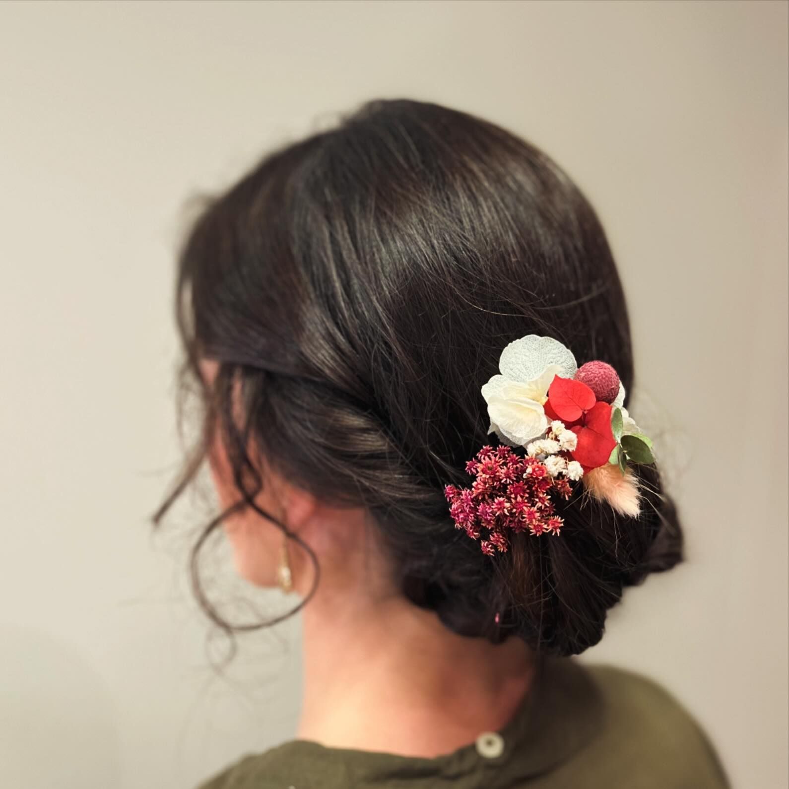 Mujer con cabello oscuro recogido, adornado con un tocado floral de flores rojas, blancas y rosas.