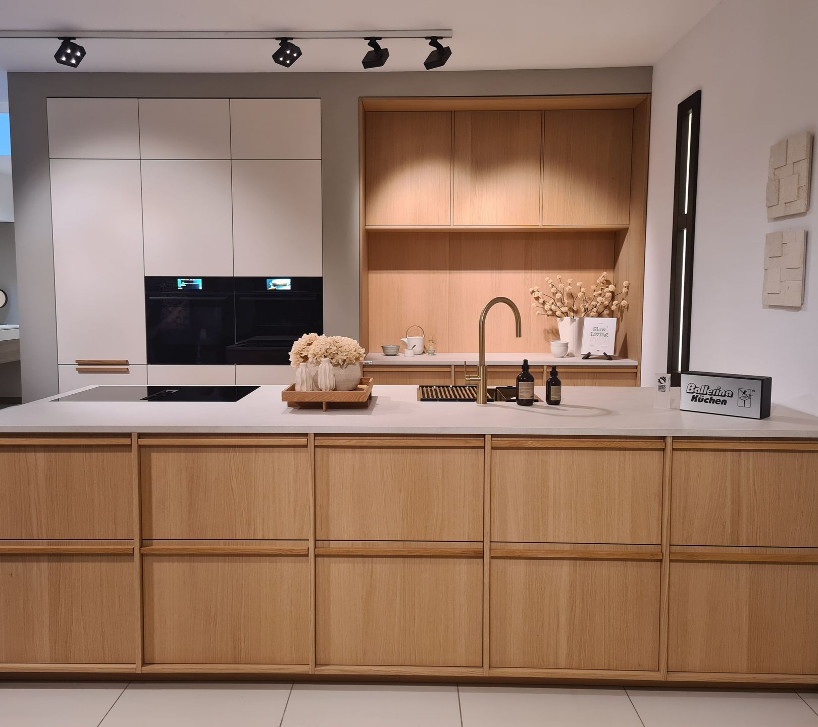 Cuisine moderne avec placards en bois clair, plans de travail blancs, four encastré et évier.