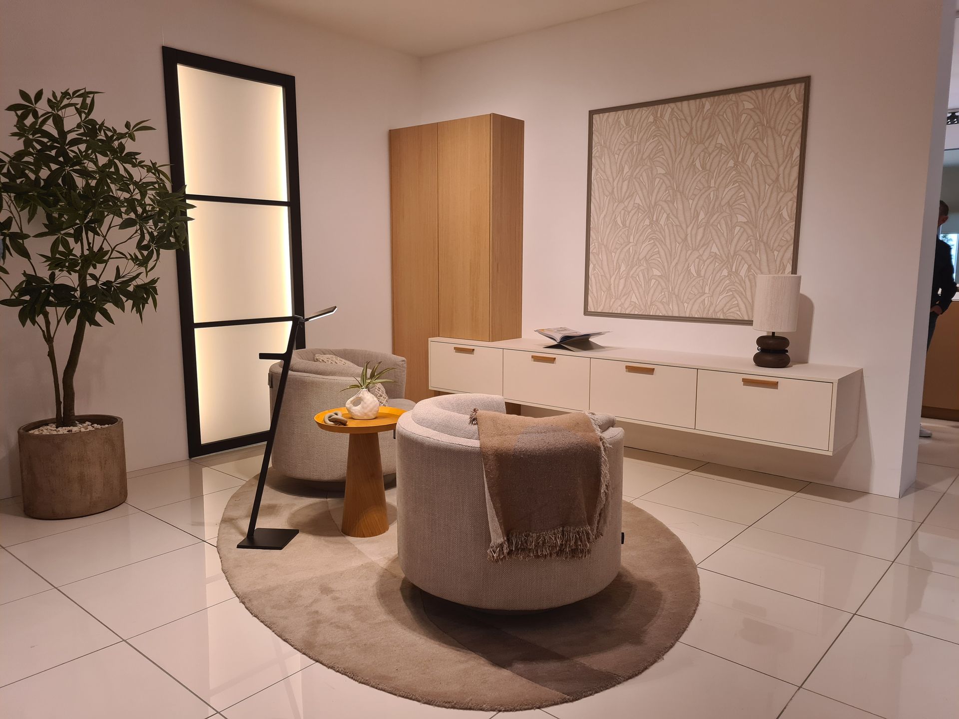 Salon minimaliste avec placards blancs, fauteuil rond beige, meuble en bois et plante en pot.