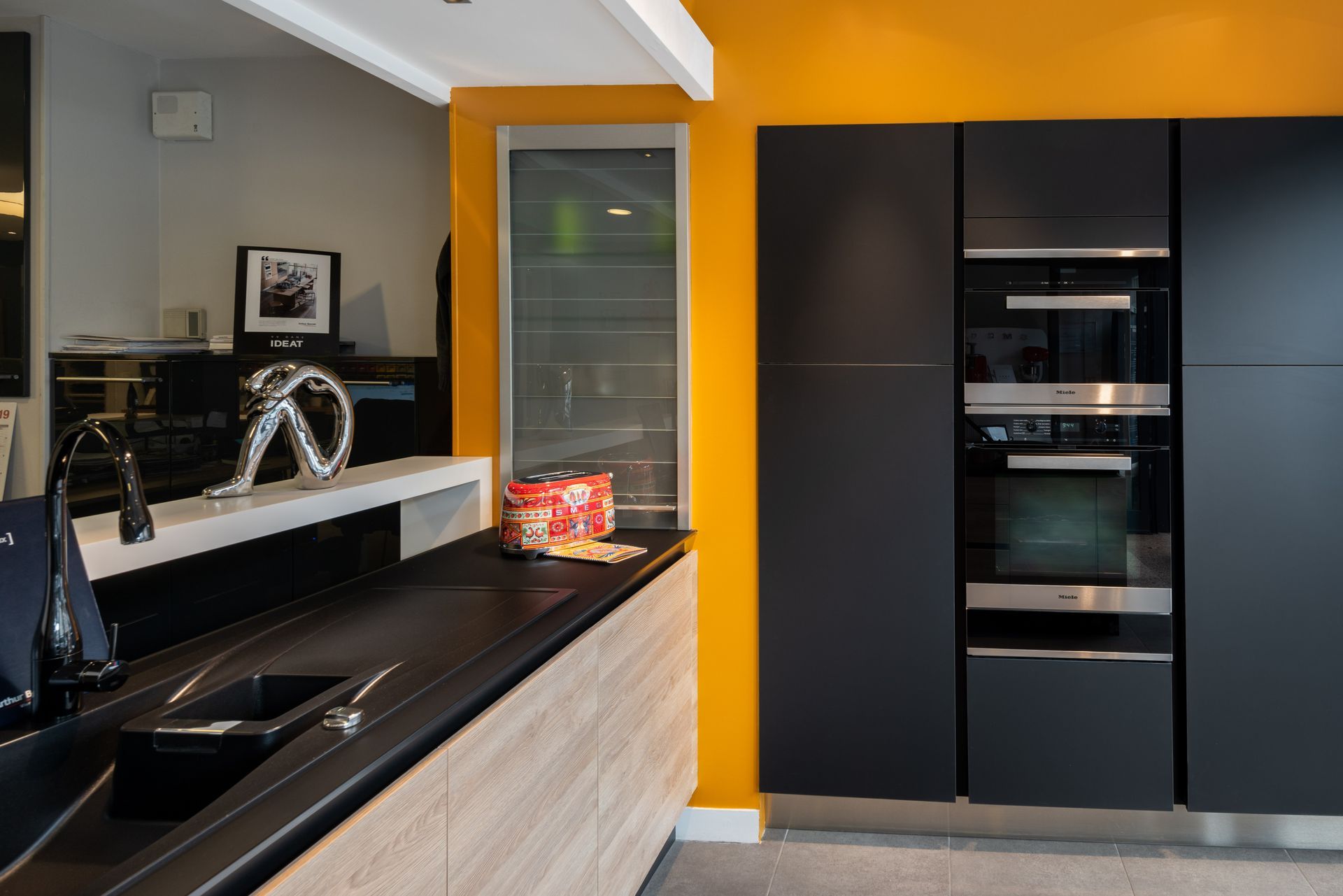 Cuisine moderne avec comptoirs noirs, mur d'accent orange et four et réfrigérateur encastrés.