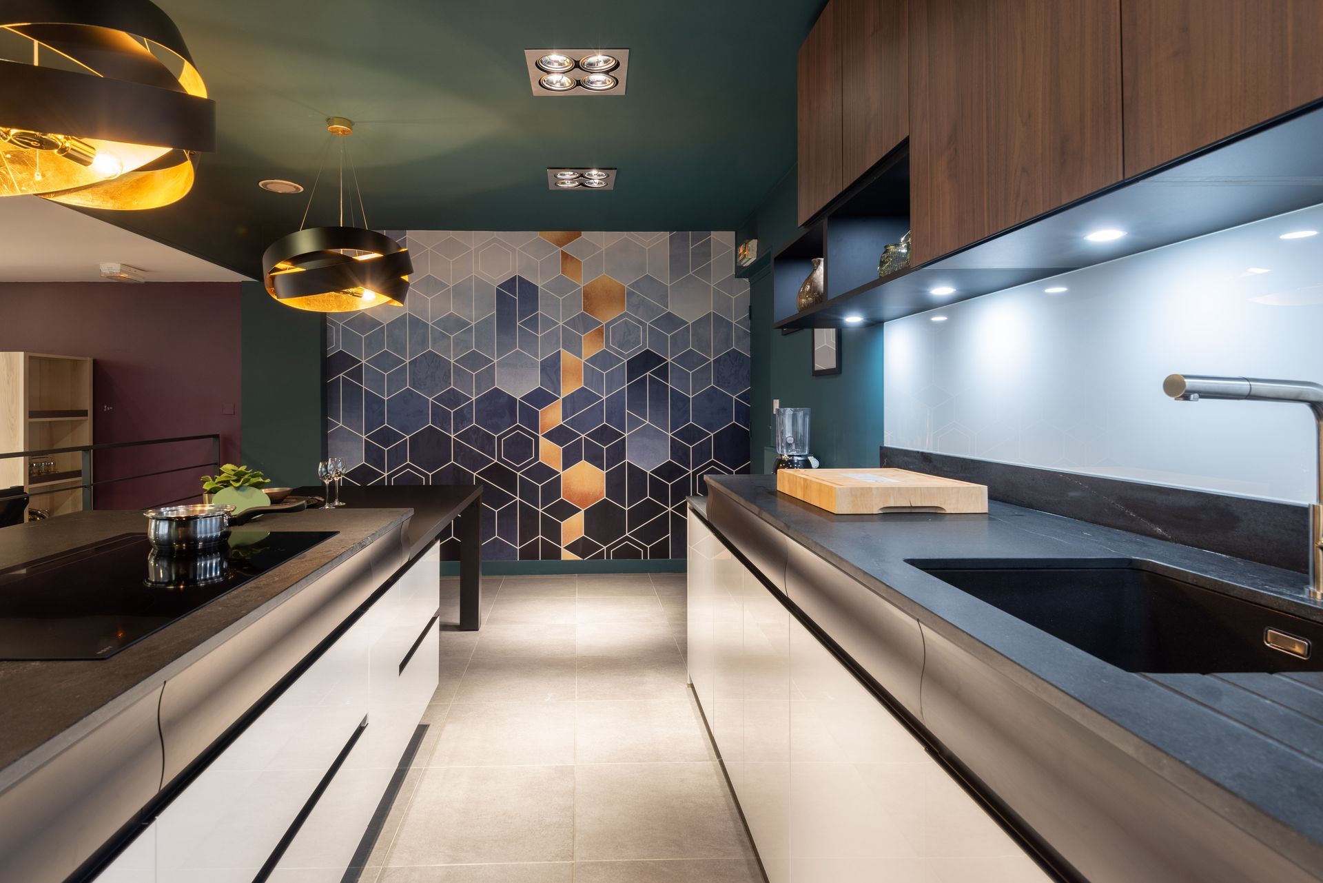 Intérieur de cuisine moderne avec placards en bois foncé, comptoirs noirs et crédence en carreaux hexagonaux bleus.