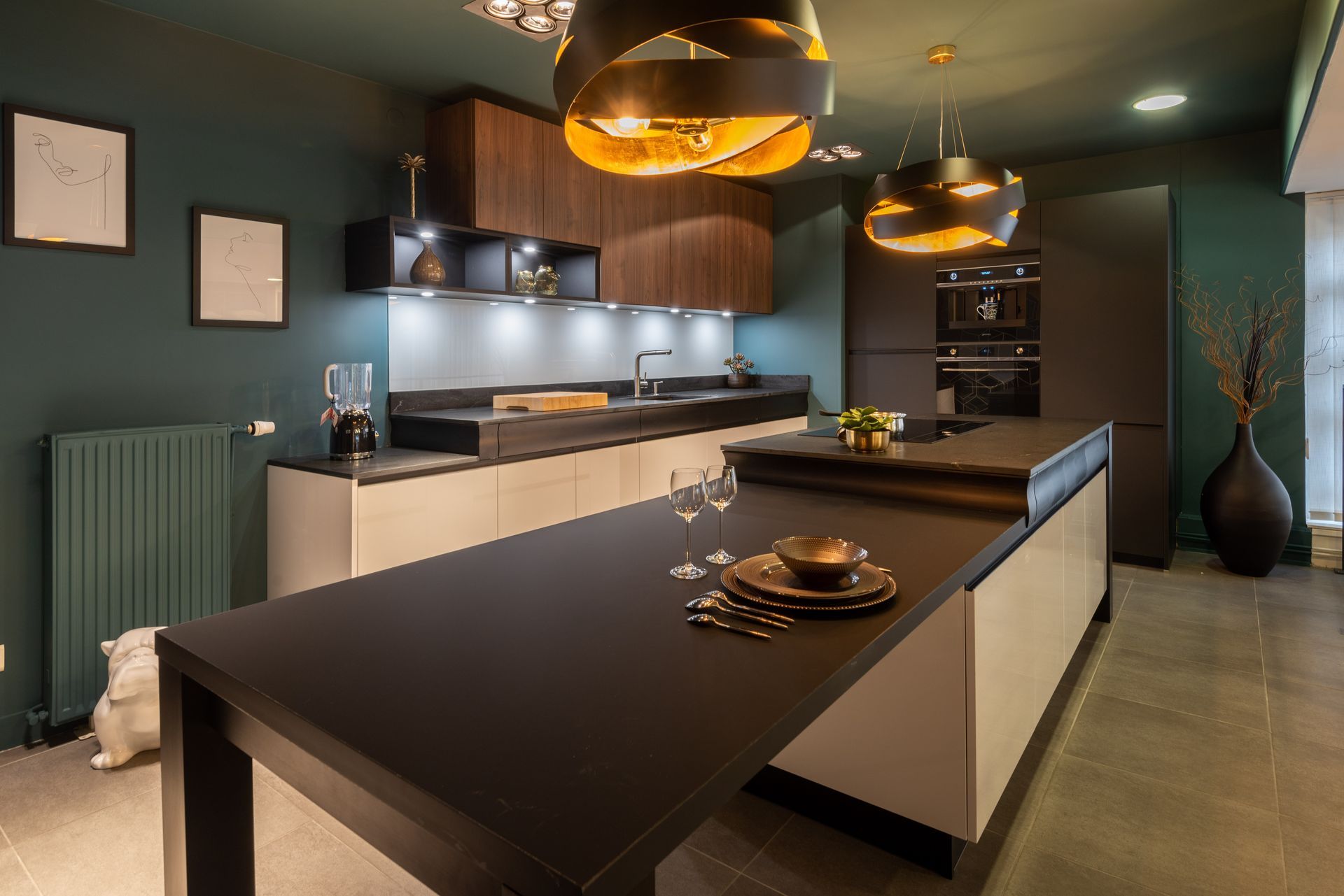 Cuisine moderne avec îlot noir, suspensions lumineuses, électroménager en inox et murs vert foncé.