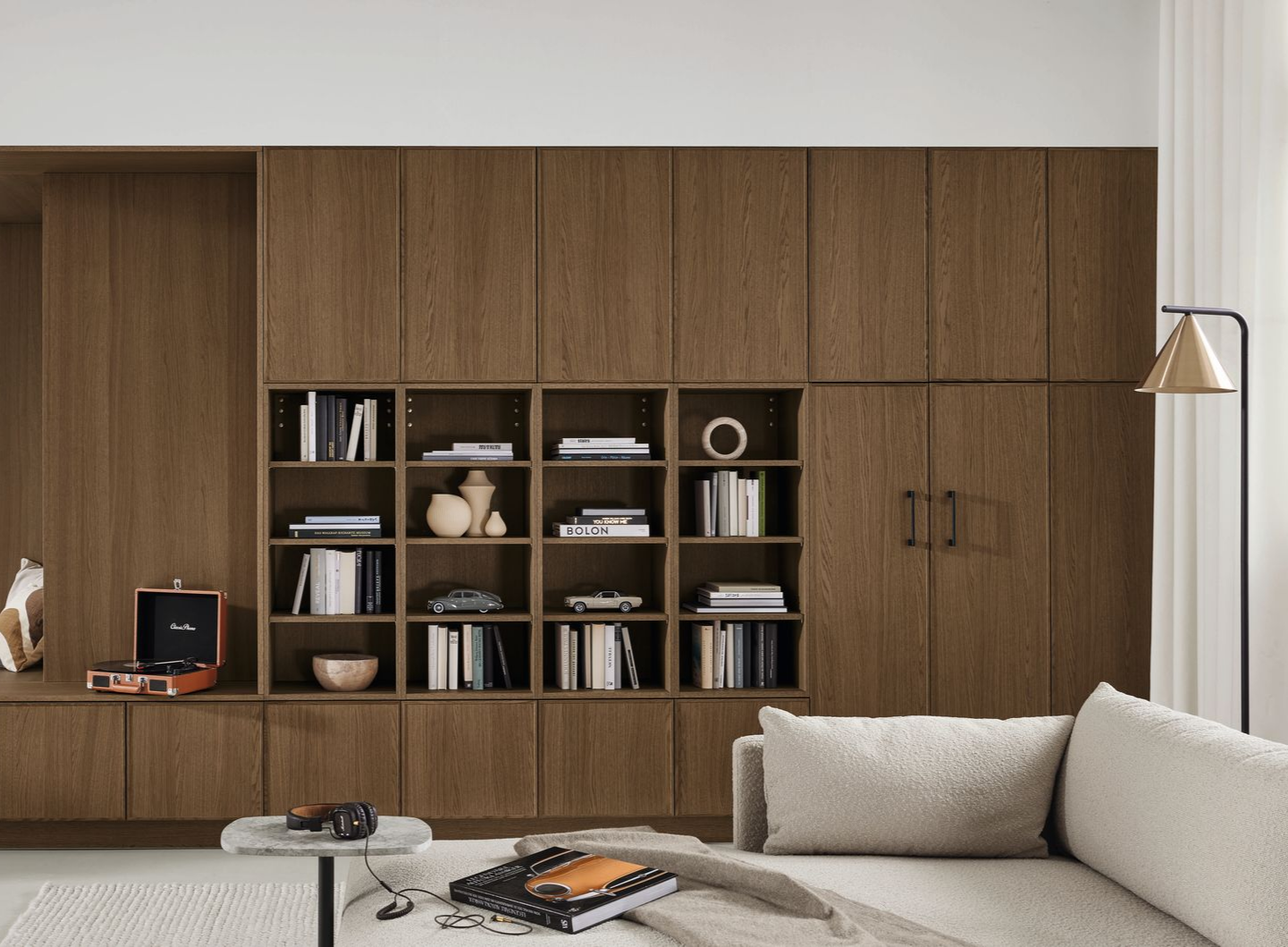 Salon moderne avec meubles muraux en bois, étagères ouvertes, canapé, table basse et lampadaire.
