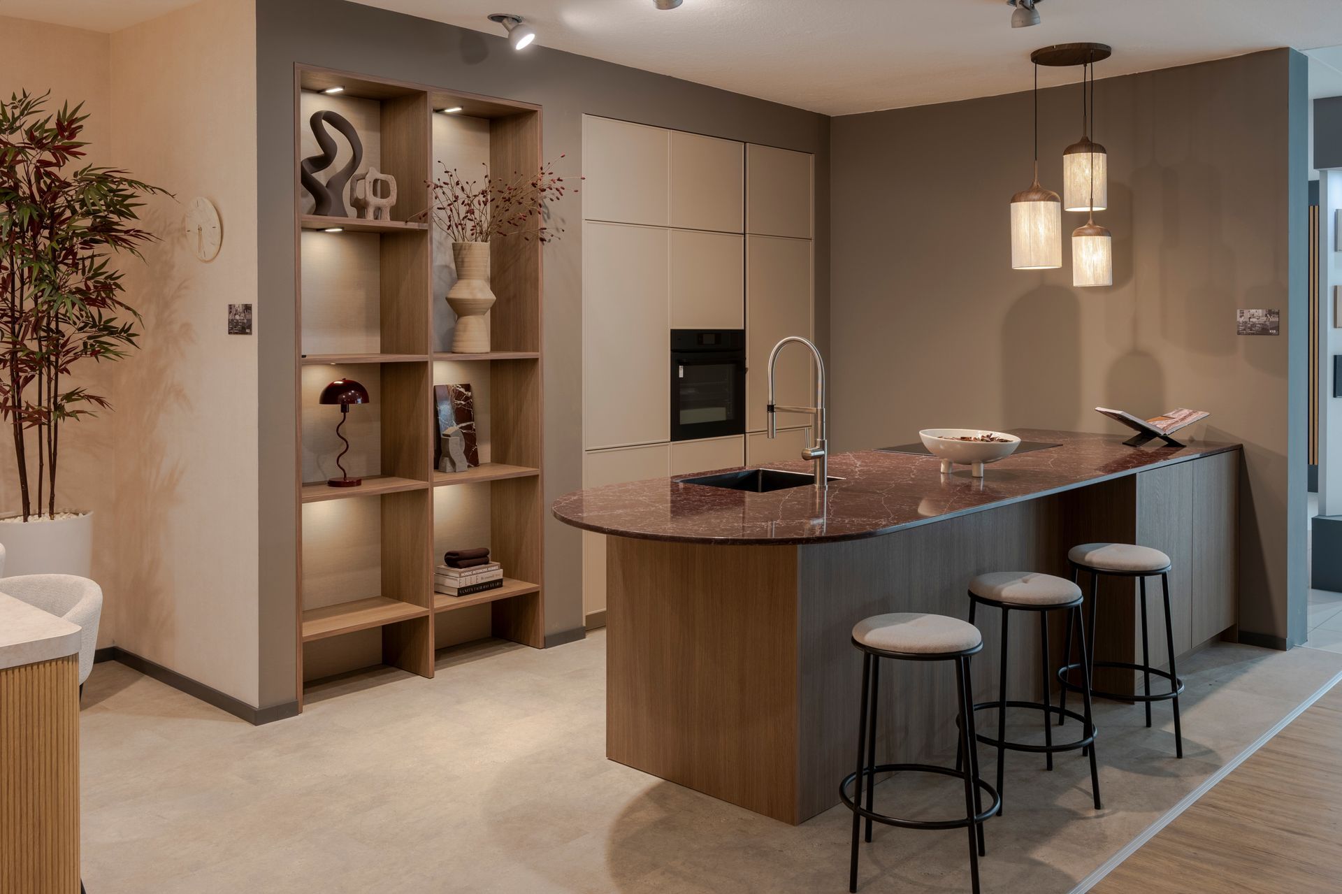 Cuisine moderne avec îlot incurvé, tabourets de bar, suspensions lumineuses et étagères intégrées.