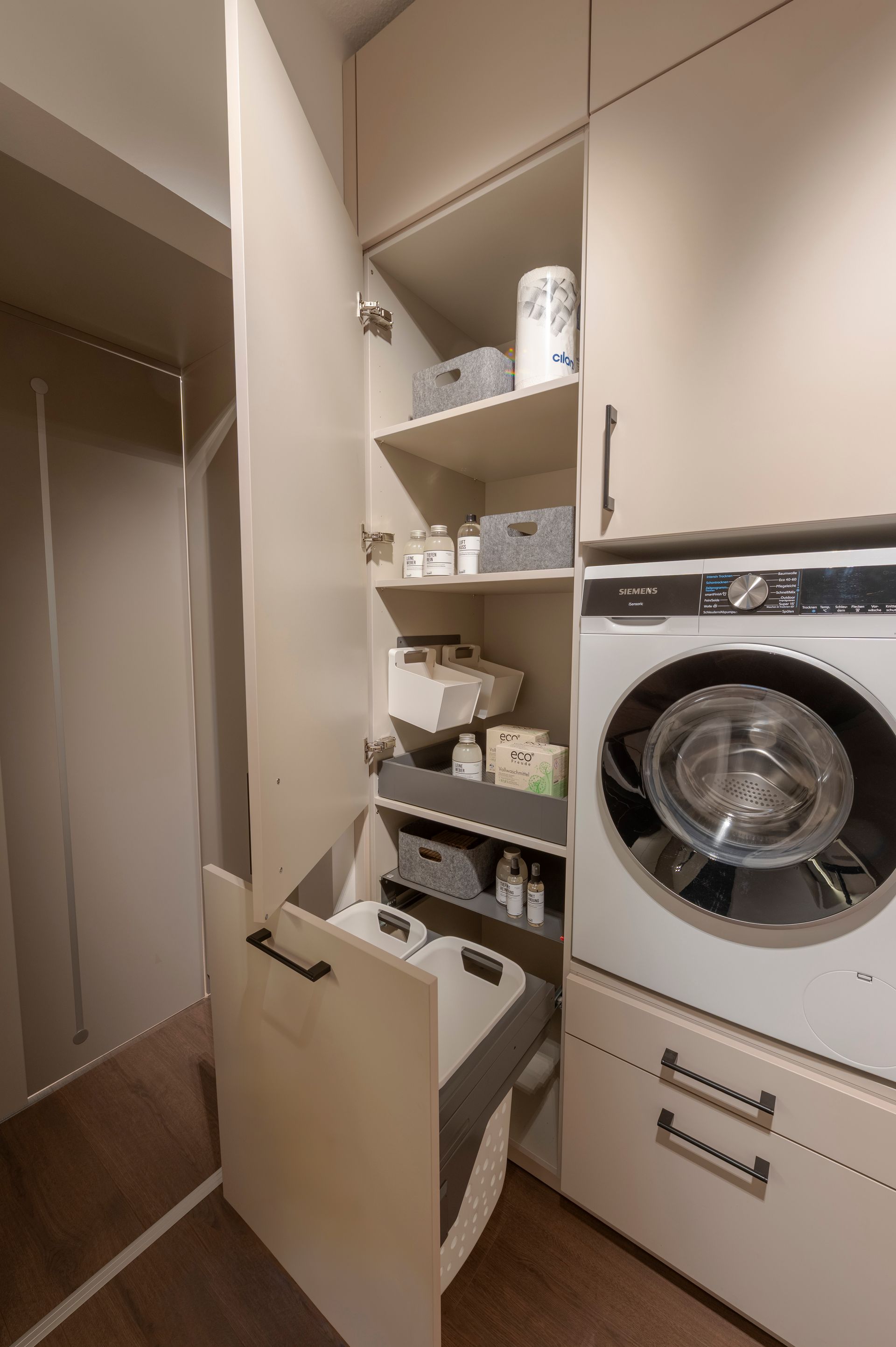 Petite buanderie avec lave-linge superposé, étagères ouvertes et murs et placards blancs.