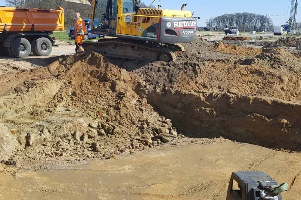 Ein Bagger gräbt Erde auf einer Baustelle aus, ein Muldenkipper steht in der Nähe.