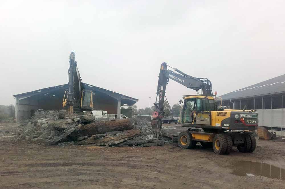 Zwei Bagger reißen ein Gebäude ab; grauer, bedeckter Himmel.