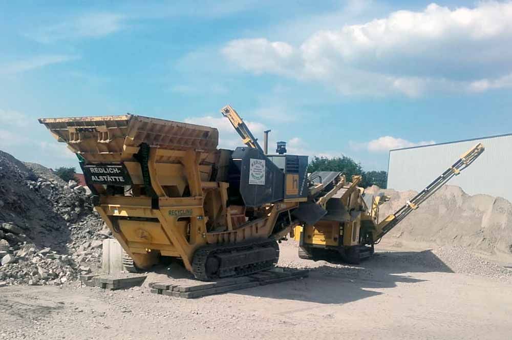 Gelbe Industriemaschine auf Ketten, die Material zerkleinert, im Freien.