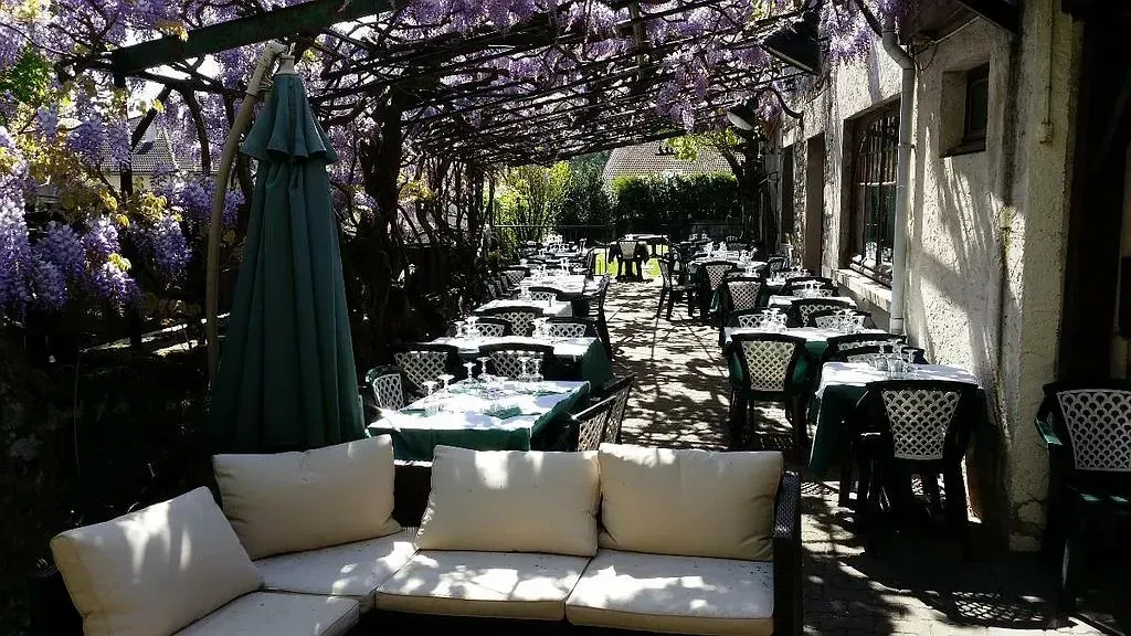 Photo de la terrasse du restaurant avec les tables dressées, le salon de jardin et un parasol sur la gauche.