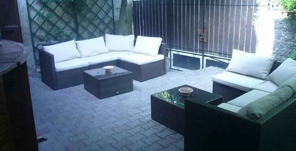 Photo de deux salons de jardin sur une terrasse, entourée de murs et d'un portail noir.