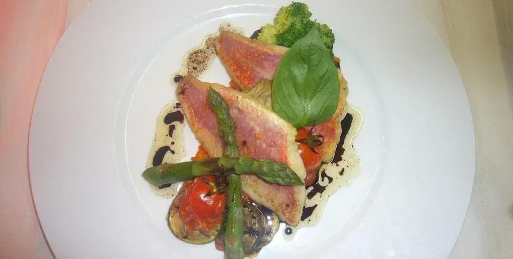 Photo d'un plat dressé avec du poisson, de la sauce, des tomates et des asperges.