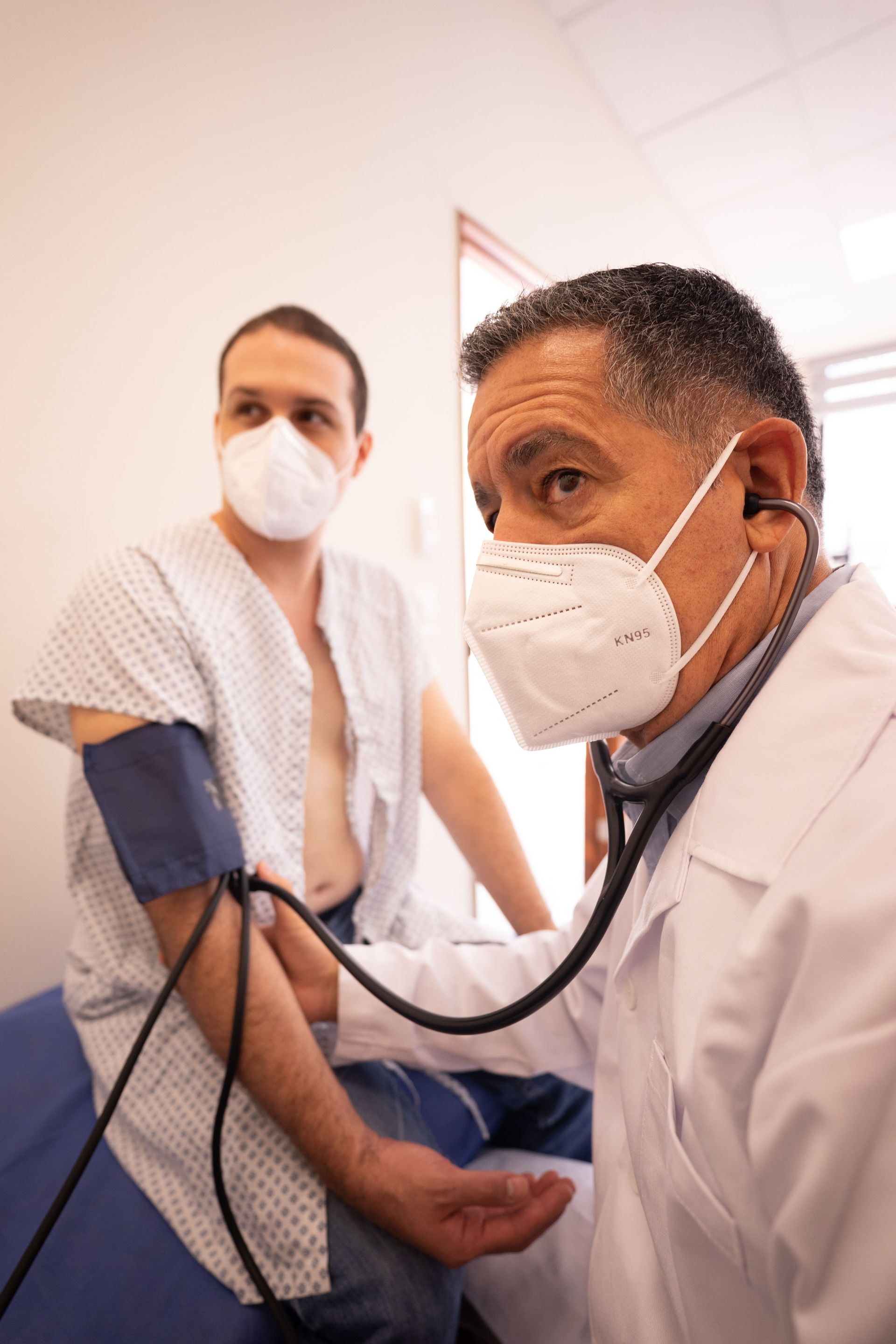 Un médico toma la tensión arterial a un paciente con mascarilla en una sala de consulta