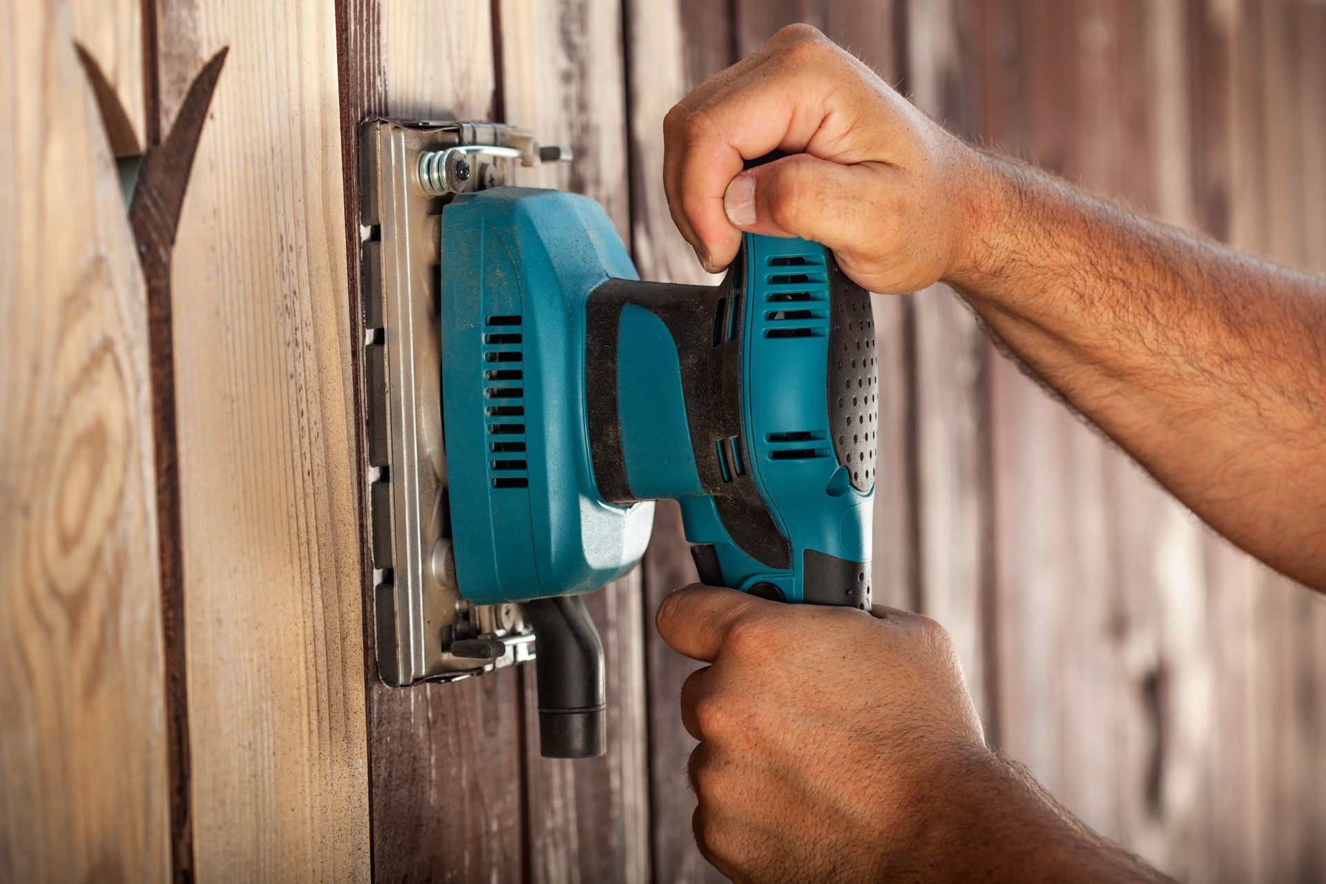 Des mains tenant une perceuse électrique turquoise contre une serrure de porte en bois.