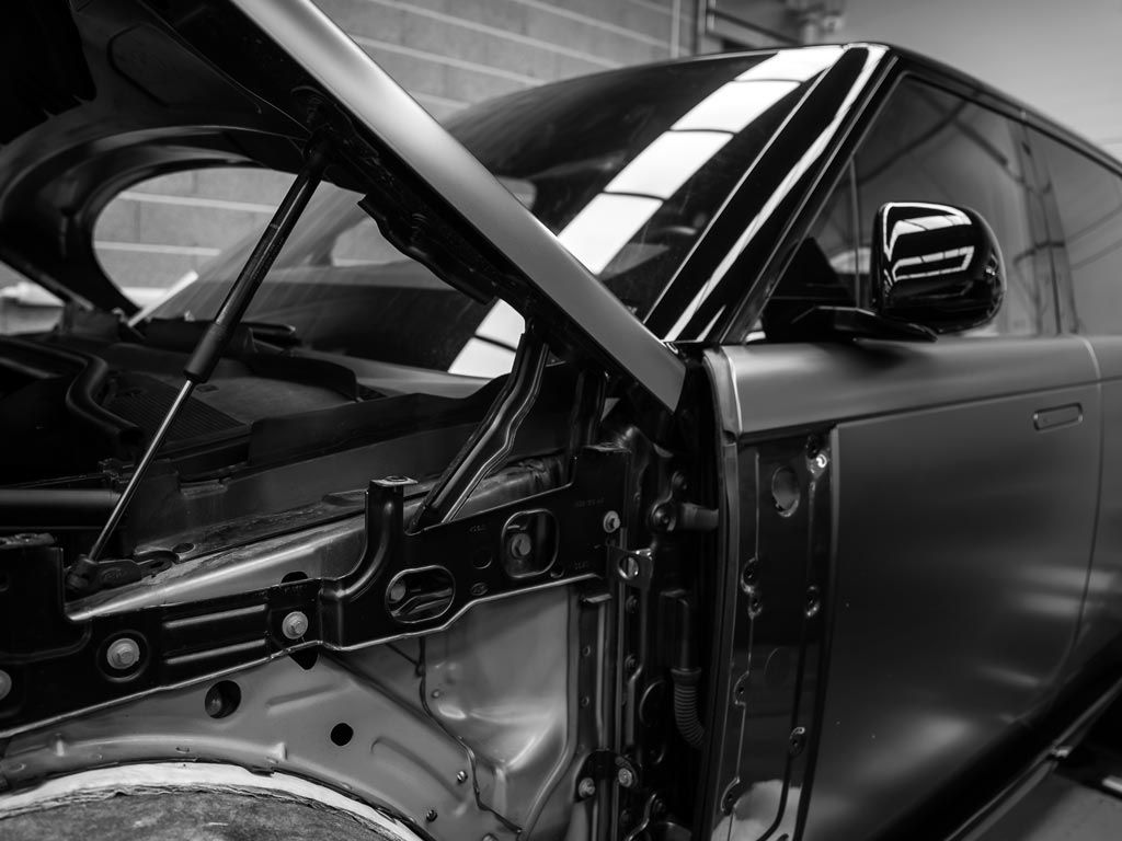 Gros plan en noir et blanc d'une voiture capot ouvert, montrant le compartiment moteur et le rétroviseur extérieur.