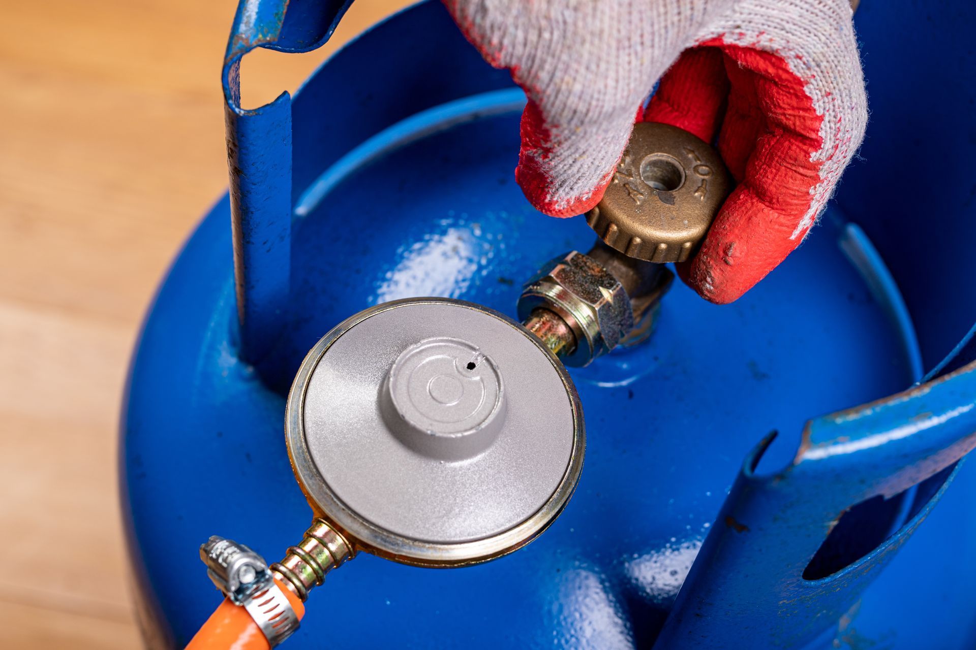 Main connectant un détendeur de bouteille de gaz à un réservoir bleu avec un gant rouge