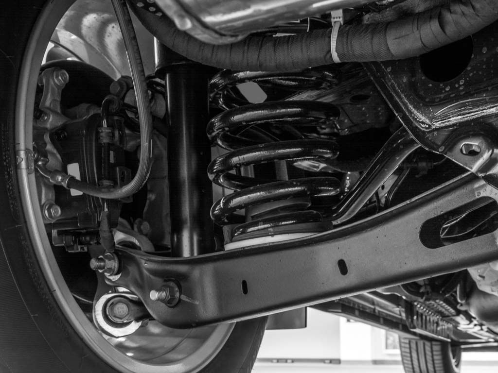 Gros plan en noir et blanc du ressort hélicoïdal et du bras de suspension d'une voiture, sous le passage de roue.