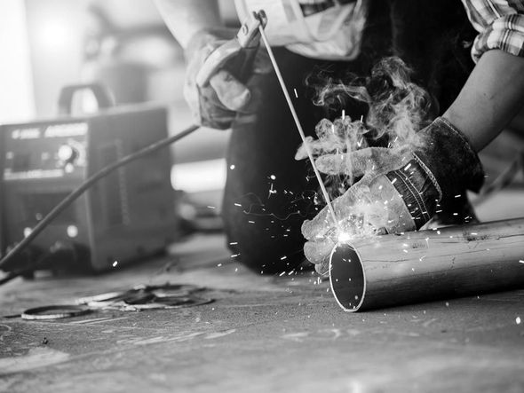 Un ouvrier soude un tuyau métallique, provoquant des étincelles et de la fumée dans un atelier.