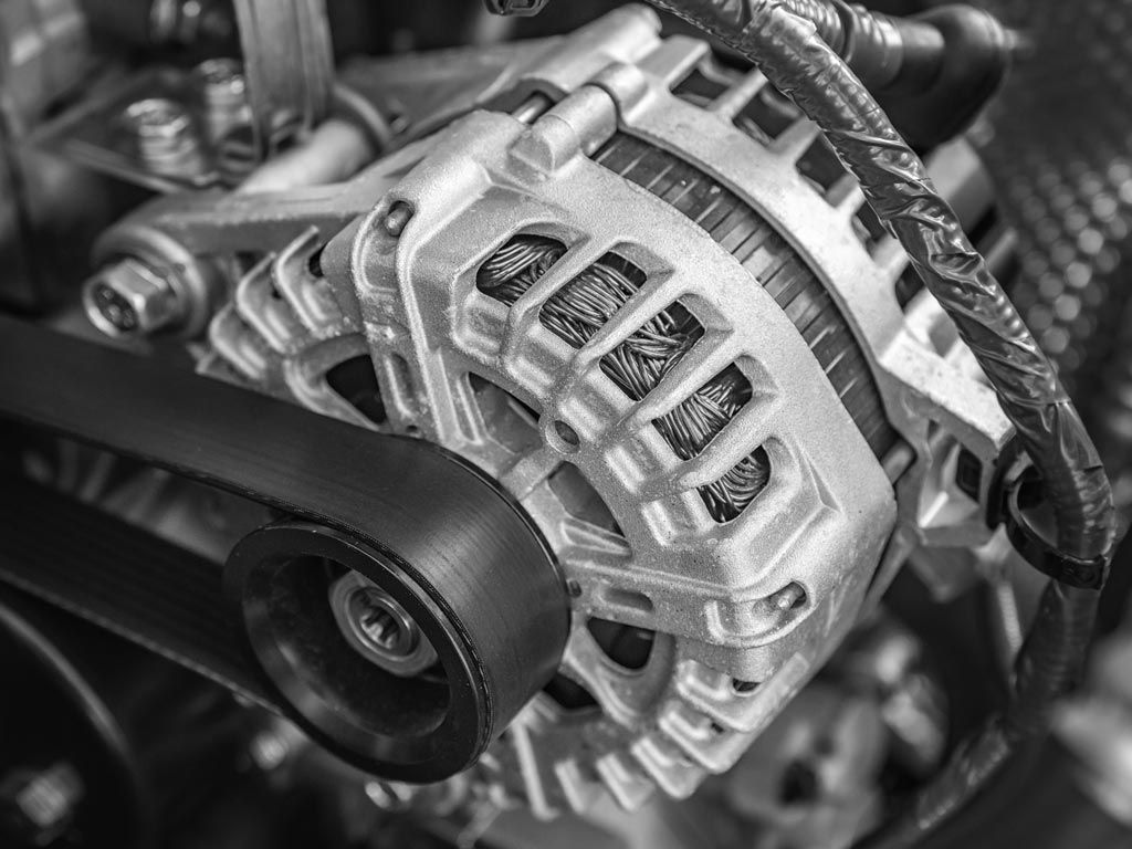 Gros plan sur un alternateur de moteur automobile avec courroie serpentine et poulies métalliques.