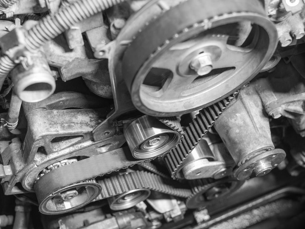 Gros plan sur un moteur avec courroies de distribution, poulies et composants métalliques.