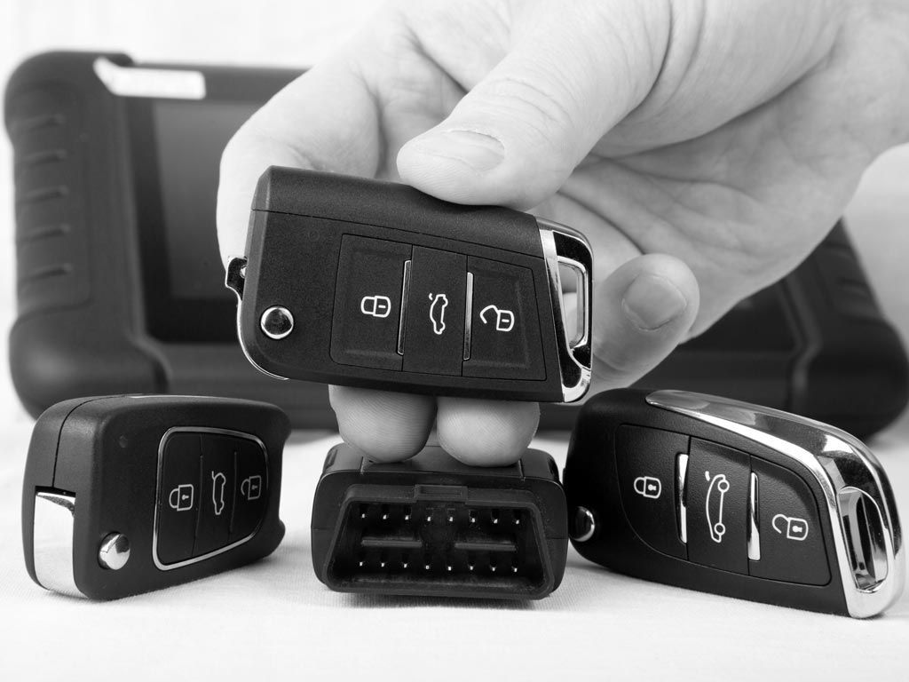 Main tenant une clé de voiture au-dessus d'une rangée de trois clés noires sur une surface blanche