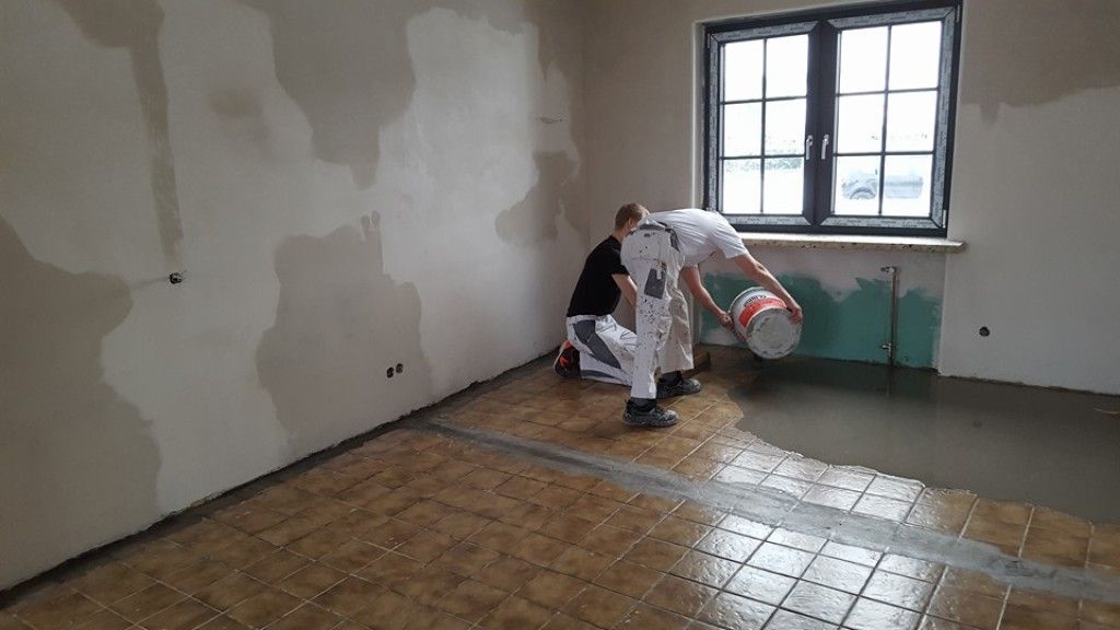 Zwei Männer verlegen Beton auf einem gefliesten Boden in einem Raum.