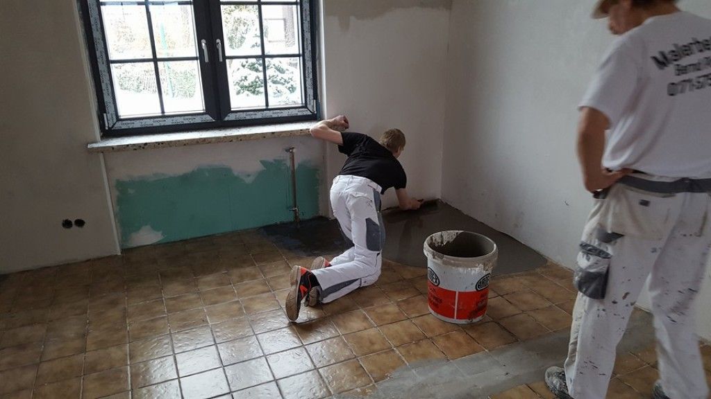 Zwei Männer arbeiten in einem Raum auf einem gefliesten Boden.