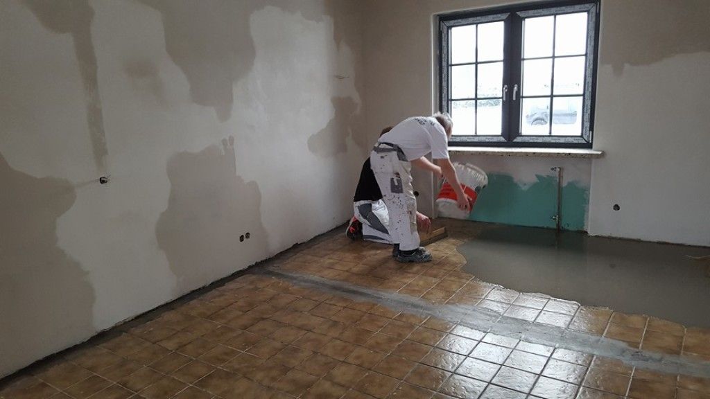 Ein Mann verlegt Beton auf einem gefliesten Boden in einem Raum.