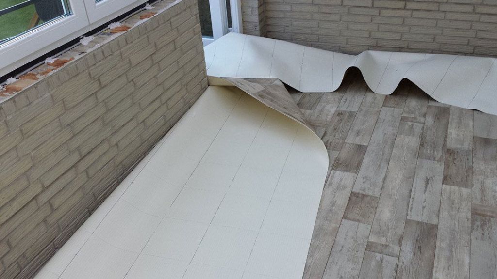 Auf einer Ziegelwand wird eine Rolle Vinylbodenbelag verlegt.