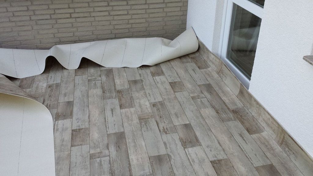 Auf einem Balkon wird eine Rolle Vinylbodenbelag verlegt.
