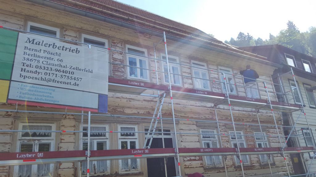 Ein Mann steht auf einer Leiter vor einem Gebäude mit Gerüst.