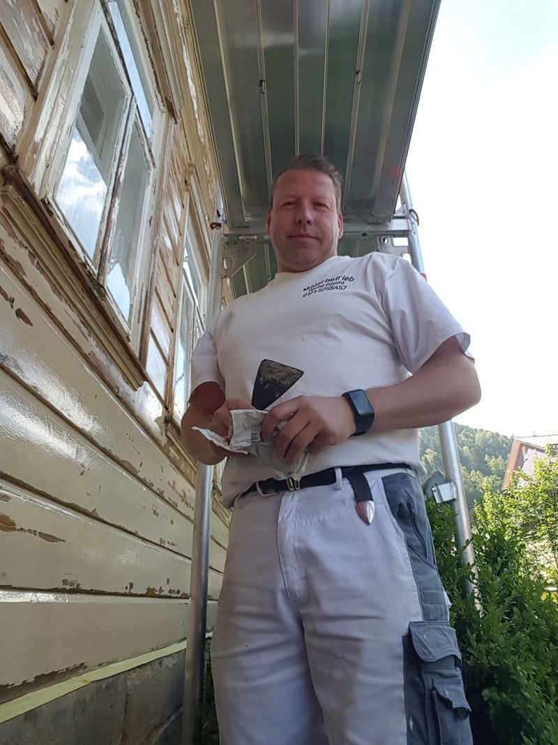 Ein Mann steht mit einem Spachtel in der Hand vor einem Gebäude.