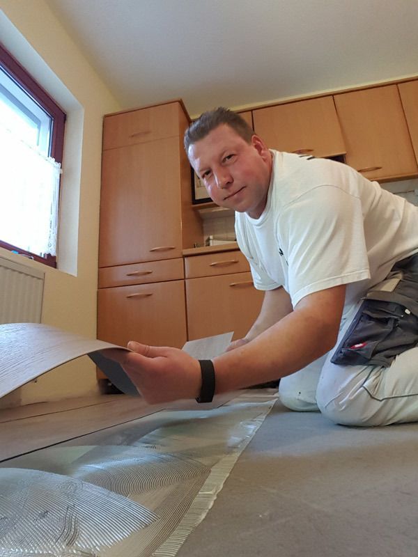 Ein Mann kniet in einer Küche und betrachtet ein Stück Vinylboden