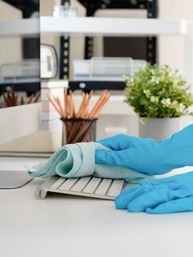 Des mains gantées de bleu essuyant le clavier d'un ordinateur portable avec un chiffon dans un environnement de bureau