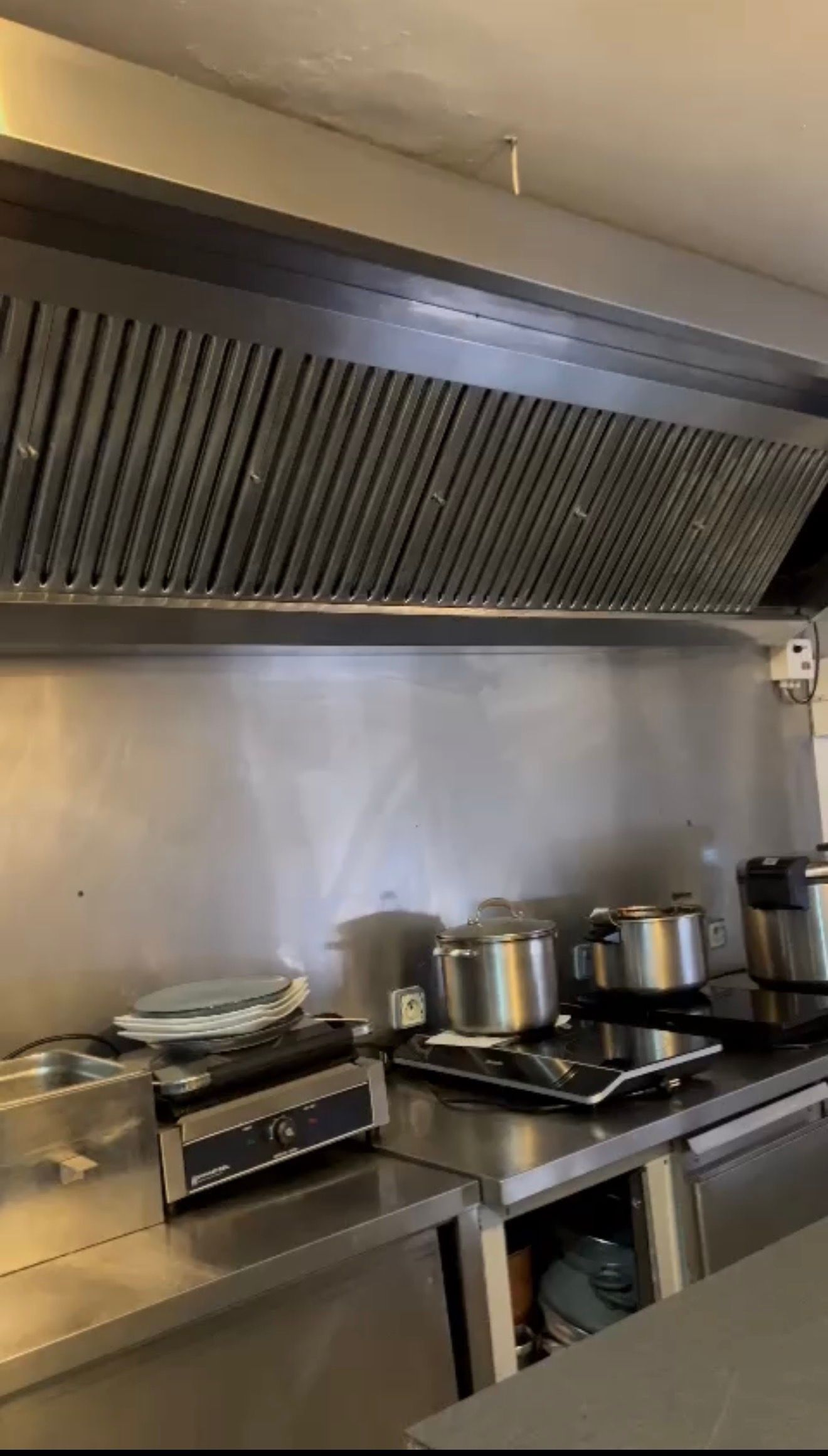 Plaque de cuisson professionnelle avec plusieurs casseroles sous une hotte en inox