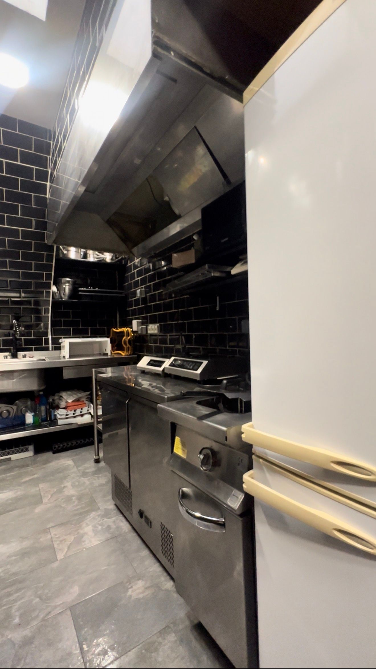 Cuisine professionnelle équipée de fours en acier inoxydable, d'une hotte aspirante et d'un espace de préparation avec un réfrigérateur blanc.