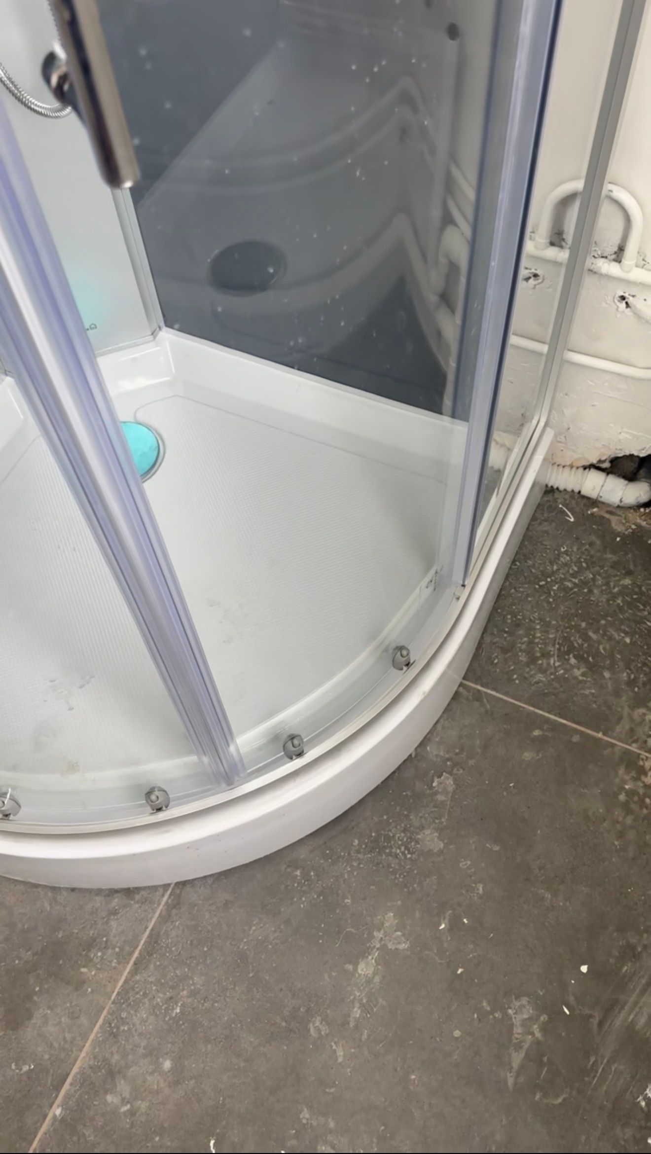 Cabine de douche en verre arrondie avec cadre argenté sur un sol de salle de bains carrelé.