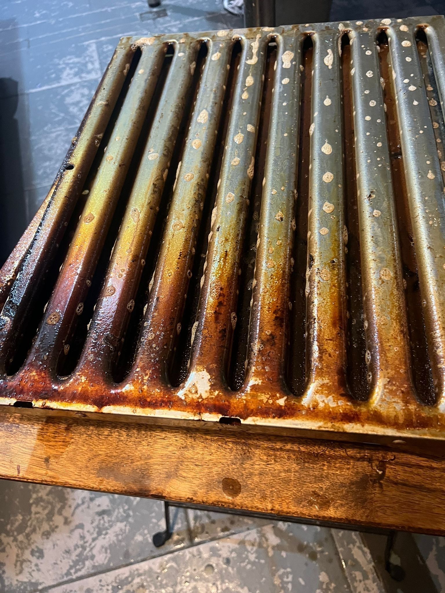 Radiateur en métal rouillé avec des rainures verticales et de la peinture écaillée sur un sol mouillé