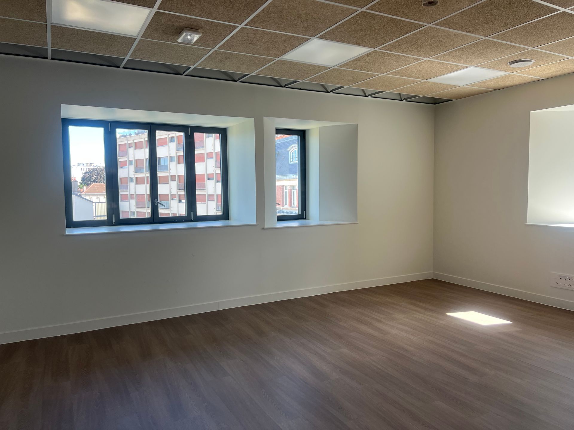 Bureau vide avec murs blancs, parquet et fenêtres laissant entrer la lumière du jour