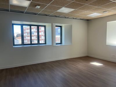 Bureau vide avec parquet, murs blancs et grandes fenêtres laissant entrer la lumière du jour
