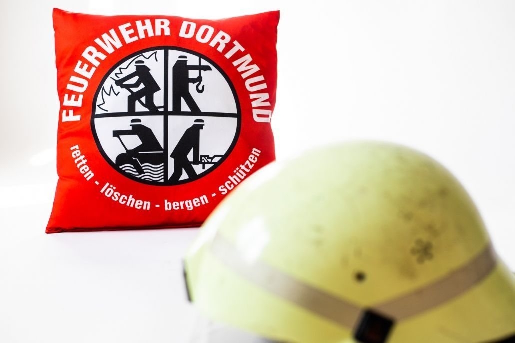 Ein gelber Helm liegt neben einem roten Kissen mit der Aufschrift Feuerwehr Dortmund