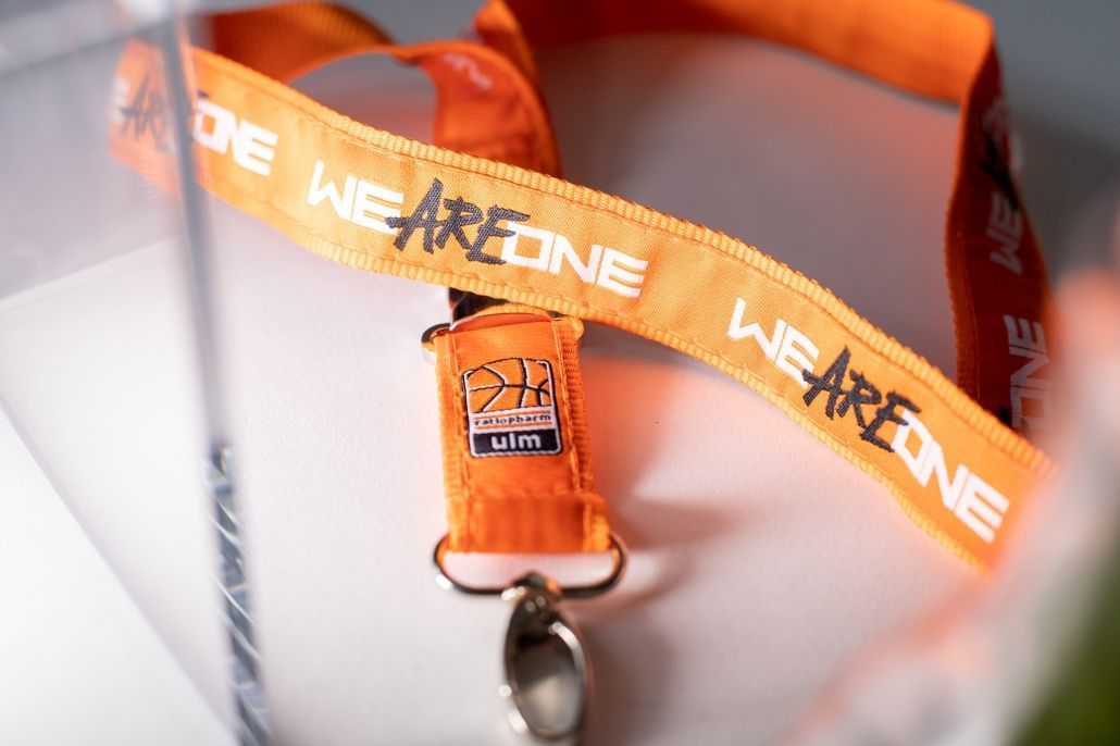 Auf einem Tisch liegt ein Schlüsselband mit der Aufschrift „Wir sind eins“.