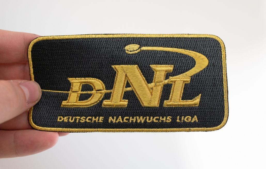 Eine Person hält einen Aufnäher mit der Aufschrift „dnl“