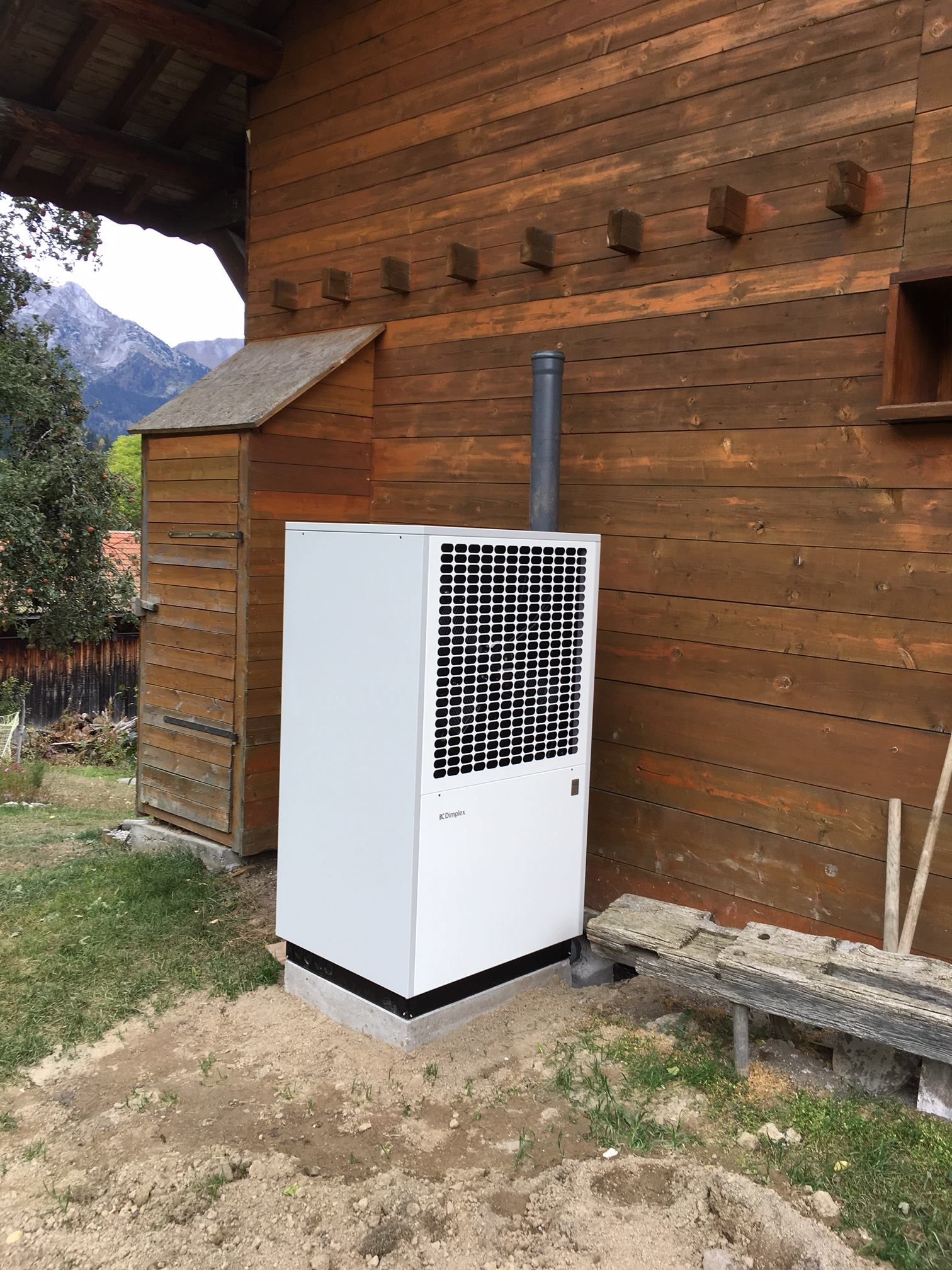 Pompe à chaleur esthétique en métal blanche derrière une maison avec bardage en bois