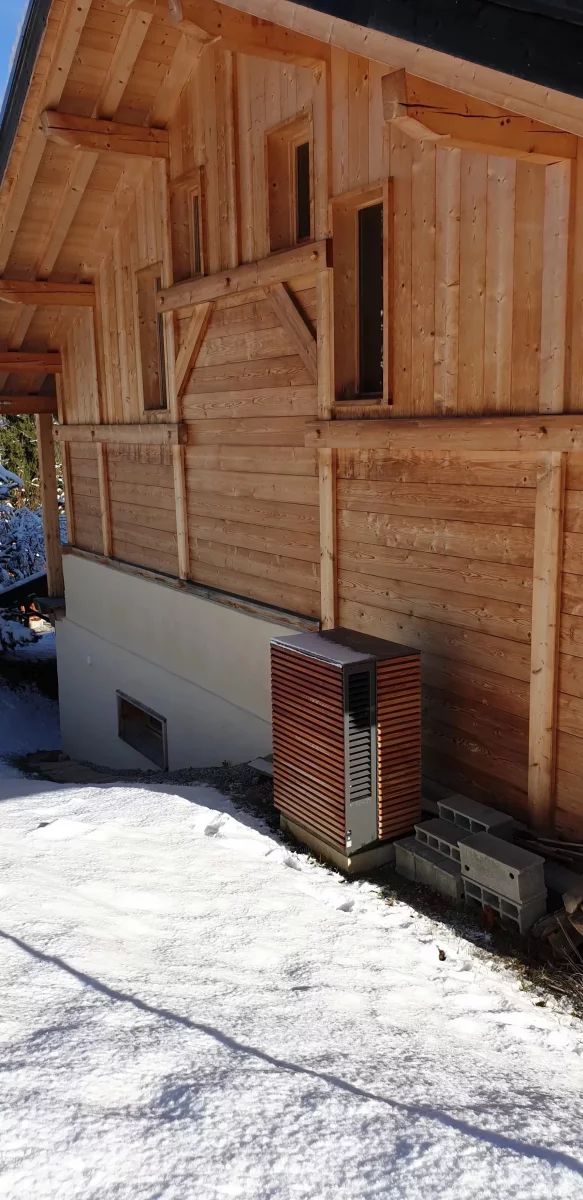 Pompe à chaleur esthétique en métal avec caisson en bois derrière un chalet dans la neige